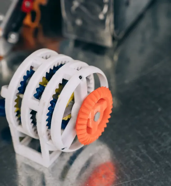 Mecanismo de engranajes blancos y naranja impreso en 3D sobre una mesa