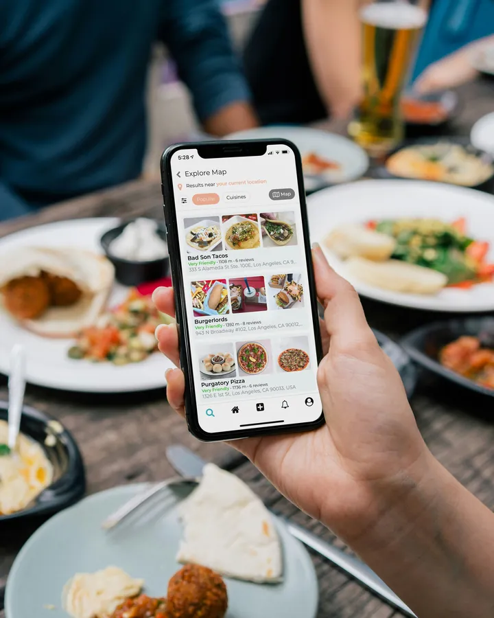 Mano sosteniendo un celular que muestra un menú digital sobre una mesa de restaurante